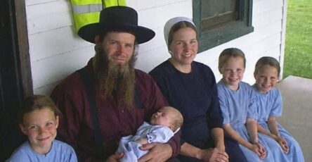 An old photograph of an Amish family standing in front of a red barn with a mysterious door in the background